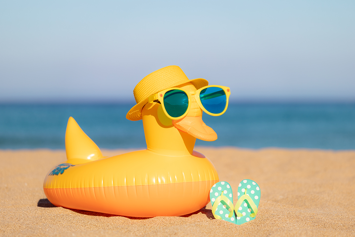 Beach flip-flops and yellow duck on the sand against blue sea an